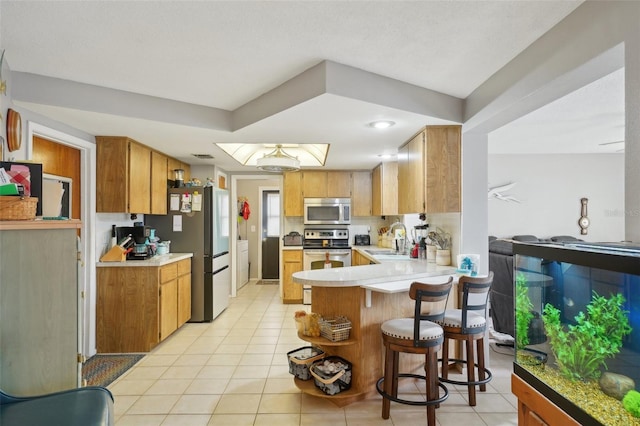 kitchen featuring kitchen peninsula, a kitchen breakfast bar, stainless steel appliances, sink, and light tile patterned floors