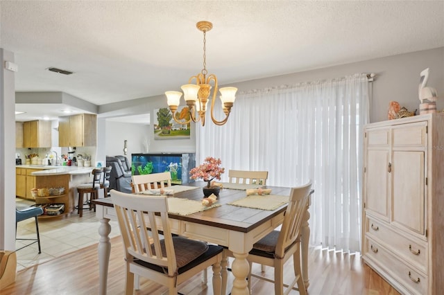 dining area featuring sink, an inviting chandelier, a textured ceiling, and light wood-type flooring