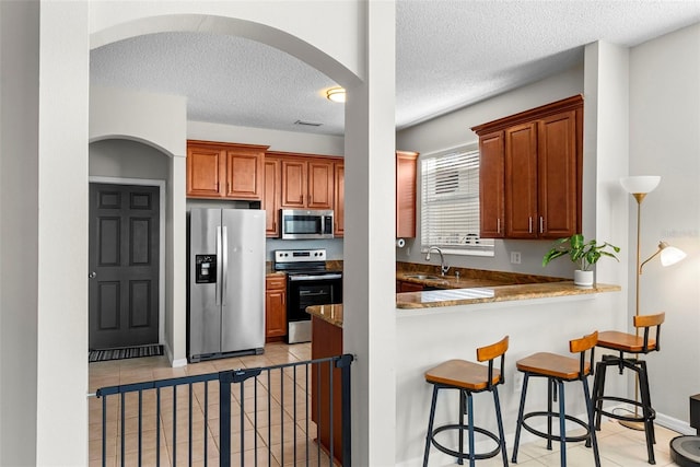 kitchen featuring sink, stainless steel appliances, kitchen peninsula, a textured ceiling, and light tile patterned flooring