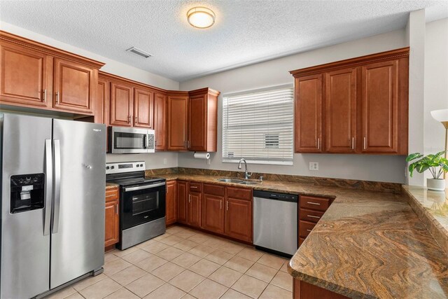 kitchen featuring dark stone counters, a textured ceiling, stainless steel appliances, sink, and light tile patterned floors