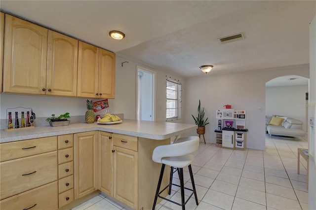 kitchen featuring kitchen peninsula, light brown cabinets, light tile patterned floors, and a kitchen breakfast bar