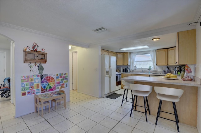 kitchen with range, a kitchen breakfast bar, white fridge with ice dispenser, light brown cabinetry, and kitchen peninsula