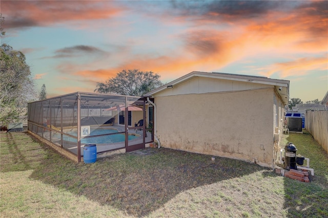 back house at dusk featuring a lanai, a yard, and a fenced in pool