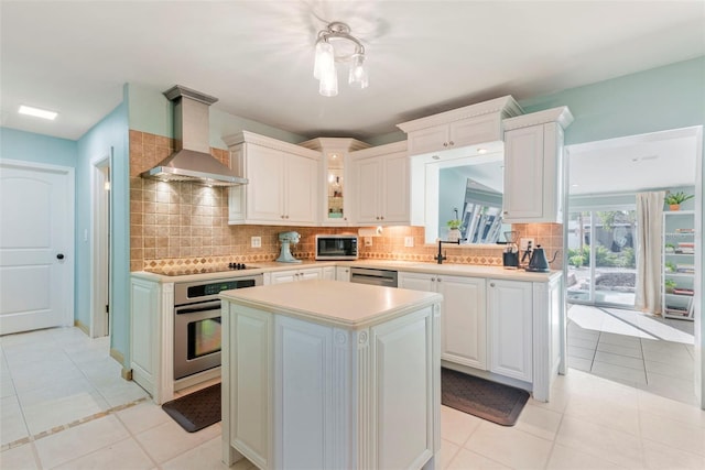 kitchen featuring stainless steel appliances, a kitchen island, wall chimney range hood, and white cabinetry