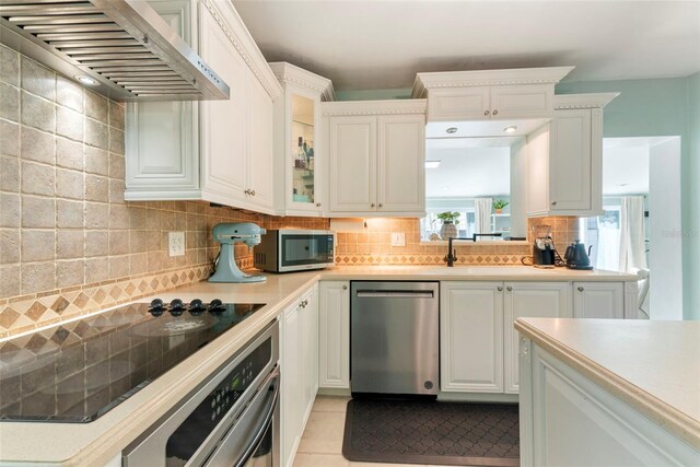 kitchen with wall chimney exhaust hood, stainless steel appliances, light tile patterned floors, tasteful backsplash, and white cabinetry