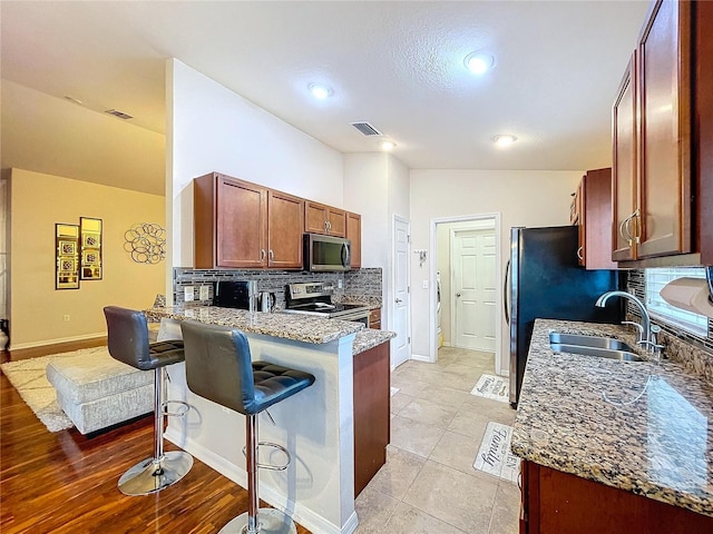 kitchen with a breakfast bar, lofted ceiling, sink, kitchen peninsula, and stainless steel appliances