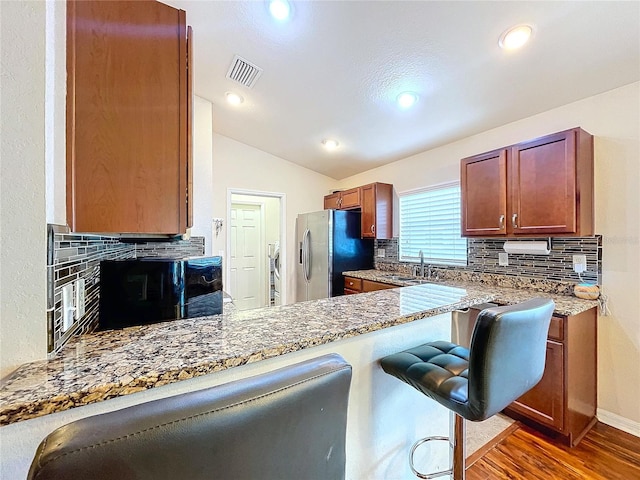 kitchen featuring dark wood-type flooring, a kitchen breakfast bar, kitchen peninsula, vaulted ceiling, and stainless steel fridge with ice dispenser