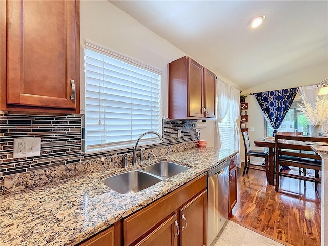 kitchen with decorative backsplash, light stone counters, stainless steel dishwasher, vaulted ceiling, and sink