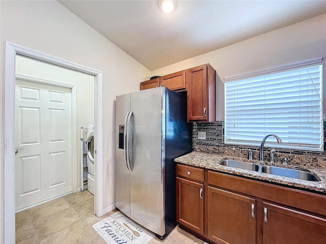 kitchen featuring sink, stainless steel refrigerator with ice dispenser, dark stone counters, lofted ceiling, and decorative backsplash