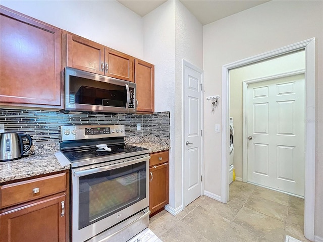 kitchen featuring stainless steel appliances, light stone counters, tasteful backsplash, and washer / clothes dryer