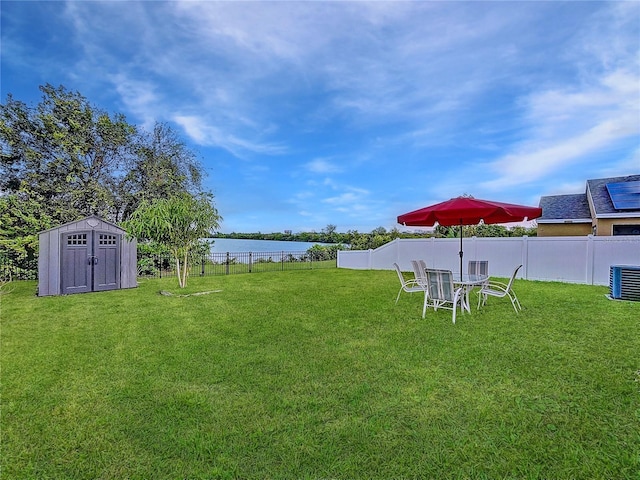 view of yard featuring central AC, a water view, and a storage unit