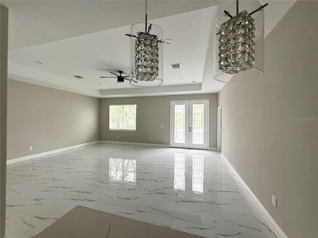 empty room with ceiling fan with notable chandelier, a raised ceiling, and french doors