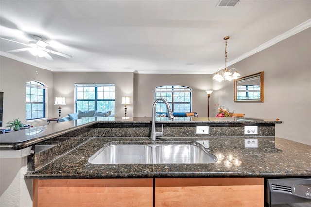 kitchen with dark stone countertops, sink, hanging light fixtures, and ornamental molding