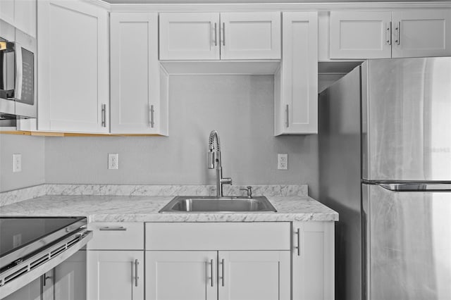 kitchen with white cabinets, appliances with stainless steel finishes, light stone counters, and sink