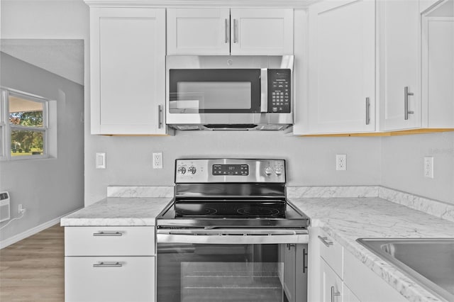 kitchen featuring sink, light stone countertops, white cabinetry, wood-type flooring, and stainless steel appliances