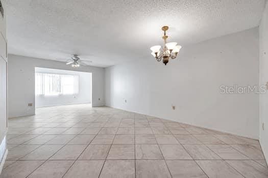 tiled spare room featuring a textured ceiling and ceiling fan with notable chandelier