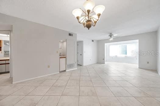 tiled empty room with ceiling fan with notable chandelier