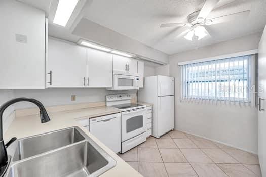 kitchen featuring white appliances, sink, ceiling fan, light tile patterned floors, and white cabinetry