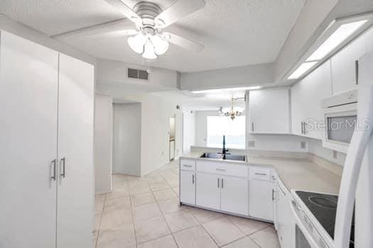 kitchen featuring ceiling fan with notable chandelier, sink, light tile patterned floors, range, and white cabinetry