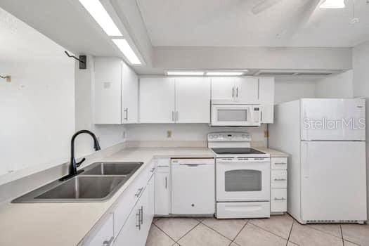 kitchen with white cabinets, light tile patterned floors, white appliances, and sink