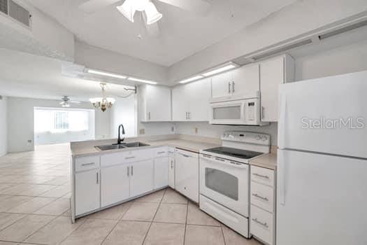 kitchen with white cabinets, white appliances, ceiling fan with notable chandelier, and sink