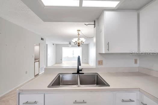 kitchen featuring white cabinetry, sink, kitchen peninsula, a chandelier, and decorative light fixtures