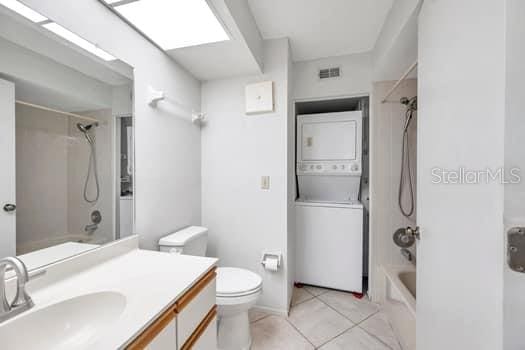 full bathroom with stacked washing maching and dryer, tiled shower / bath combo, tile patterned flooring, toilet, and vanity