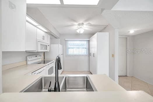 kitchen with light tile patterned flooring, sink, white cabinets, ceiling fan, and white appliances