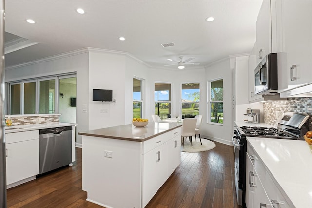 kitchen featuring decorative backsplash, stainless steel appliances, ceiling fan, a center island, and white cabinetry