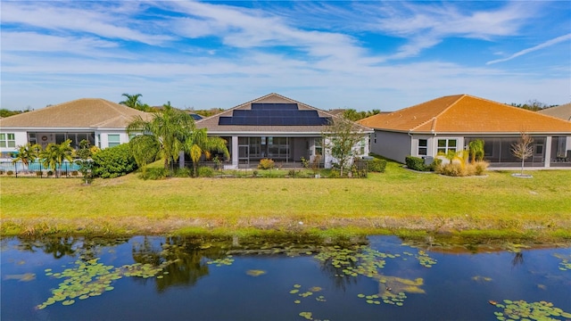 back of house featuring a sunroom, solar panels, a water view, and a yard