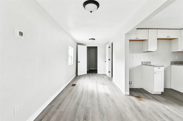 kitchen featuring white cabinets, light hardwood / wood-style flooring, and light stone countertops