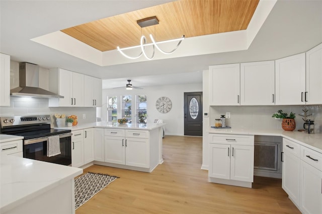 kitchen with electric stove, wall chimney range hood, decorative backsplash, decorative light fixtures, and white cabinetry