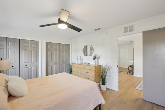 bedroom featuring ceiling fan, light hardwood / wood-style flooring, and two closets