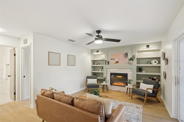 living room featuring built in shelves, light wood-type flooring, and ceiling fan