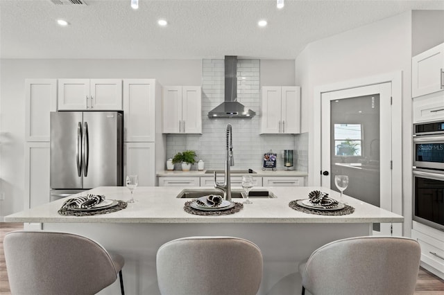 kitchen featuring a center island with sink, wall chimney exhaust hood, and appliances with stainless steel finishes