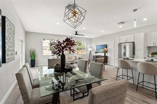 dining room with light wood-type flooring, ceiling fan with notable chandelier, and a textured ceiling