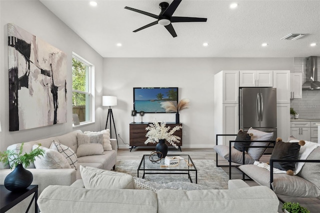 living room with ceiling fan, a textured ceiling, and light wood-type flooring