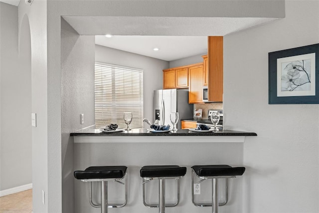 kitchen with backsplash, light tile patterned flooring, stainless steel appliances, and a kitchen breakfast bar