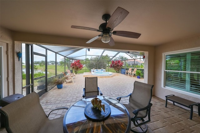 view of patio featuring ceiling fan, glass enclosure, and an in ground hot tub