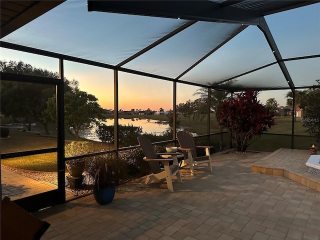 patio terrace at dusk featuring glass enclosure and a water view