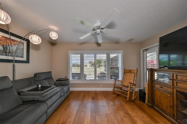 living room featuring ceiling fan, wood-type flooring, and a textured ceiling