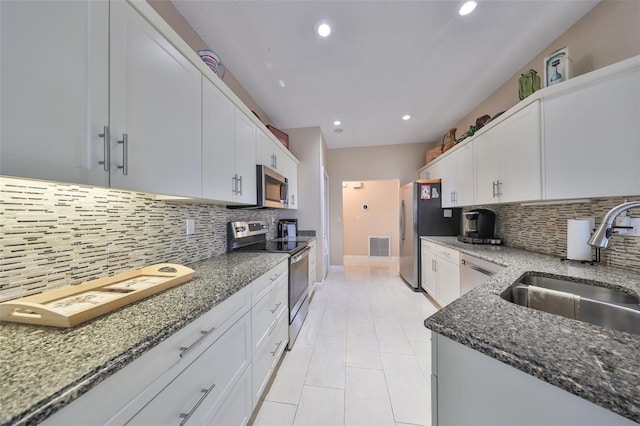 kitchen with appliances with stainless steel finishes, tasteful backsplash, dark stone counters, white cabinets, and sink