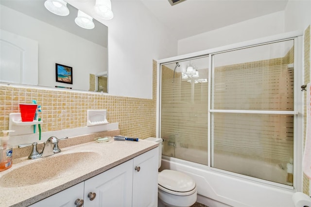 full bathroom with vanity, toilet, tile walls, and bath / shower combo with glass door