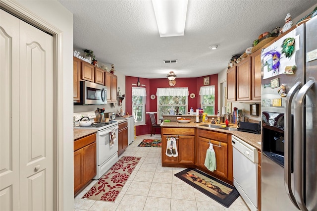 kitchen with sink, light tile patterned floors, a textured ceiling, appliances with stainless steel finishes, and kitchen peninsula