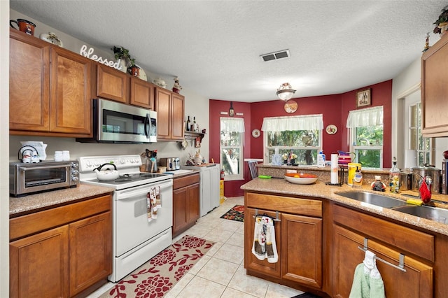 kitchen with electric range, sink, light tile patterned floors, and a textured ceiling