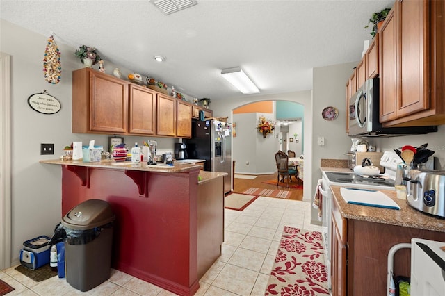 kitchen featuring range with electric stovetop, light tile patterned flooring, a kitchen bar, and a textured ceiling