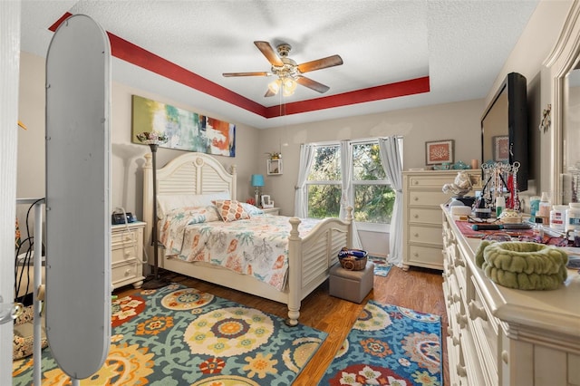 bedroom featuring ceiling fan, a raised ceiling, a textured ceiling, and light hardwood / wood-style flooring