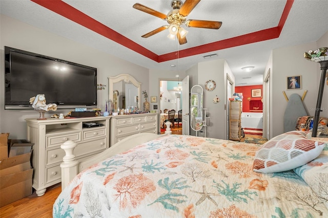 bedroom with a tray ceiling, ceiling fan, light hardwood / wood-style floors, and a textured ceiling