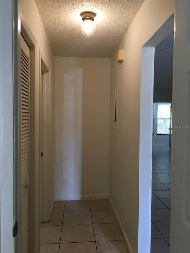 hall with a textured ceiling and light tile patterned floors