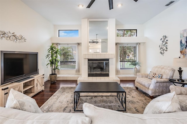 living room with a tile fireplace, dark wood-type flooring, a wealth of natural light, and a towering ceiling